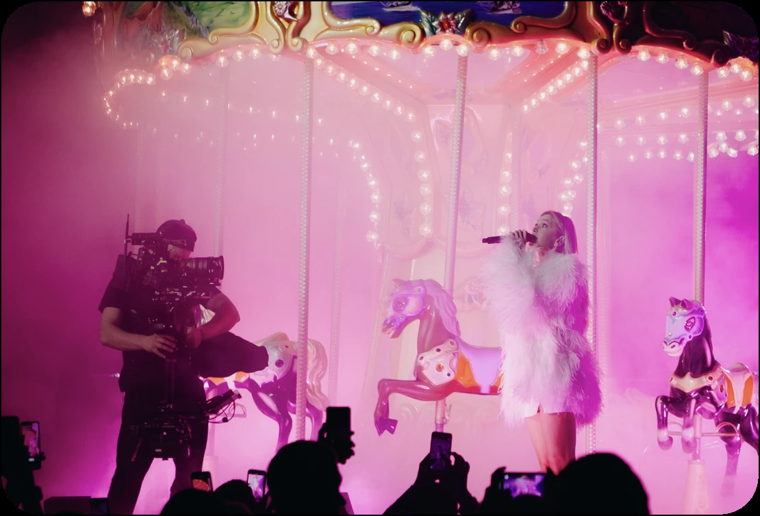 A singer performing on a pink-lit carousel while a camera operator films