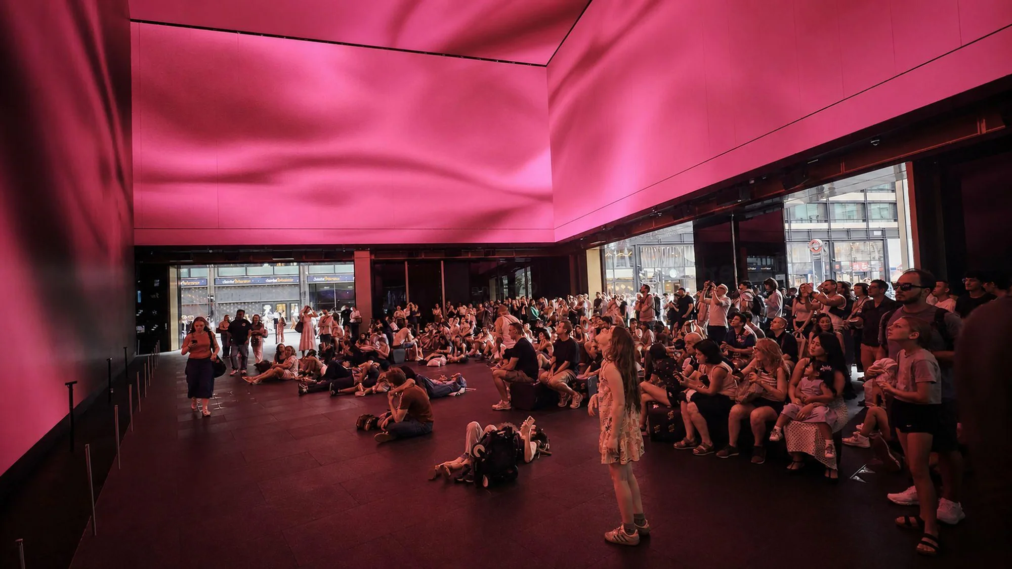 An audience gathers beneath pink fabric visuals across the ceiling.
