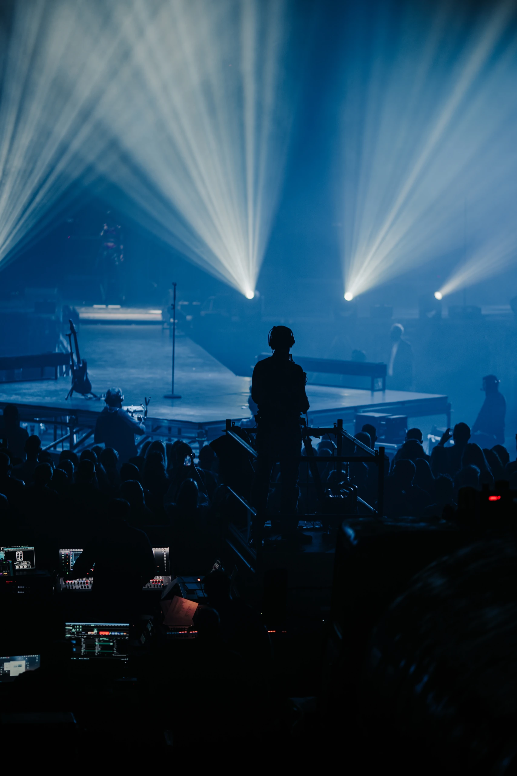 A camera operator and production desks facing the blue-lit stage