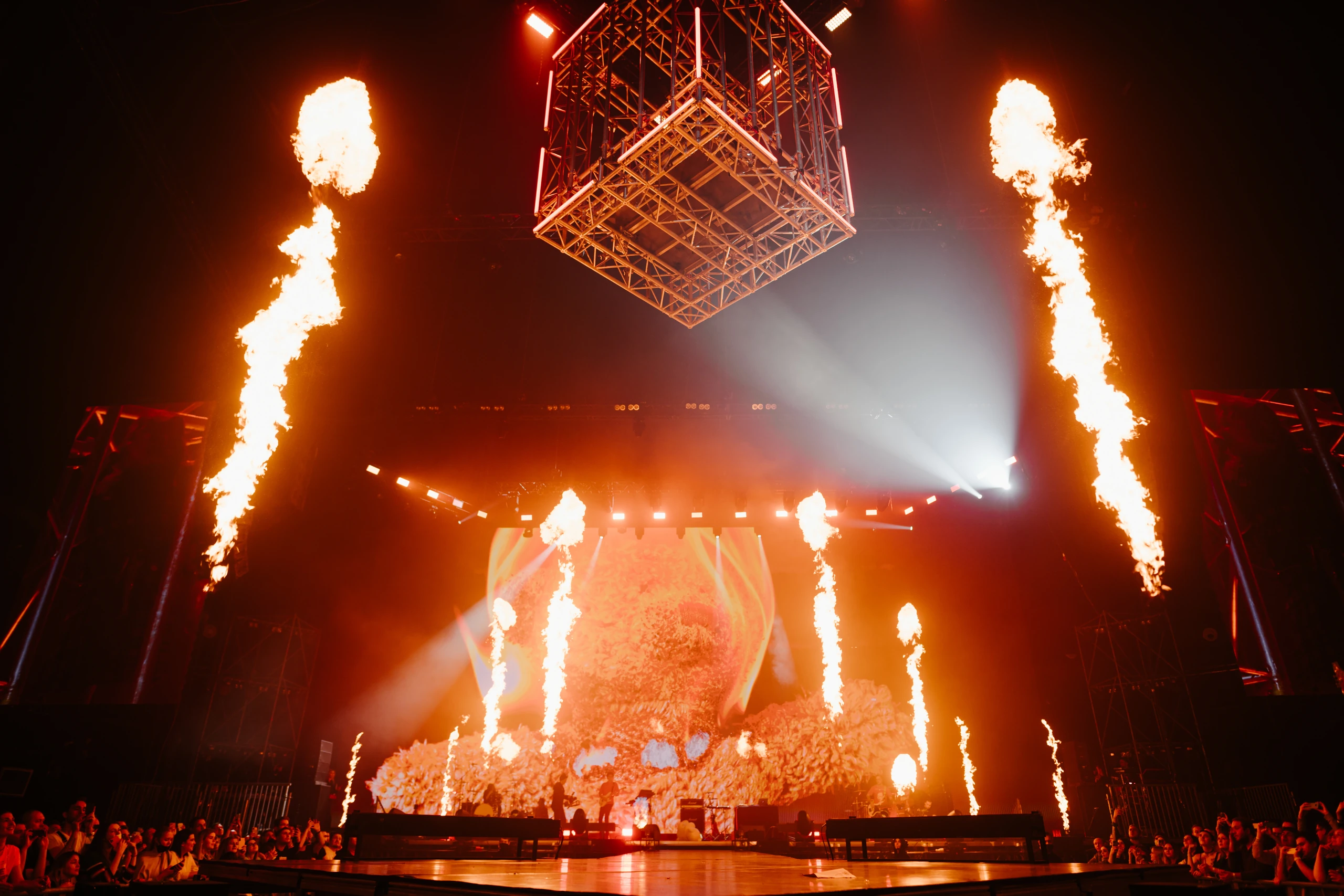 An illuminated suspended cage above the stage, framed by columns of fire